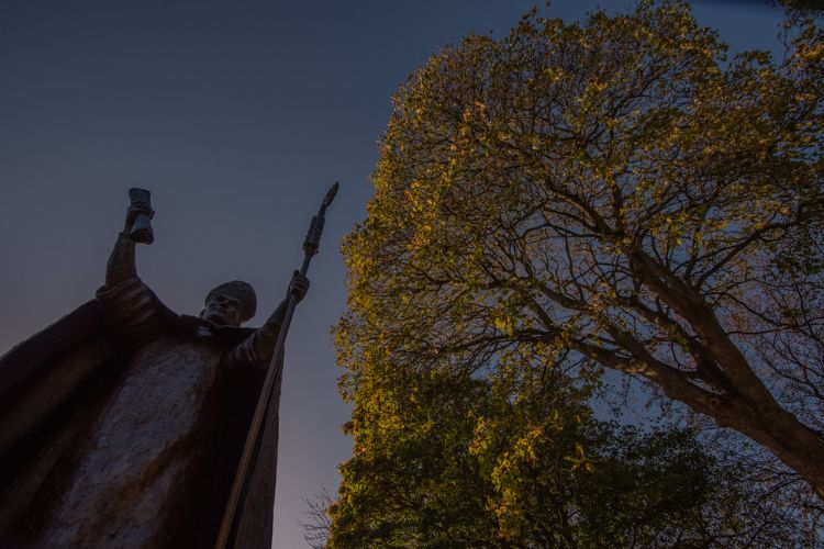 A statue of Bishop Wardlaw stands tall beside a tree in St Marys Quad